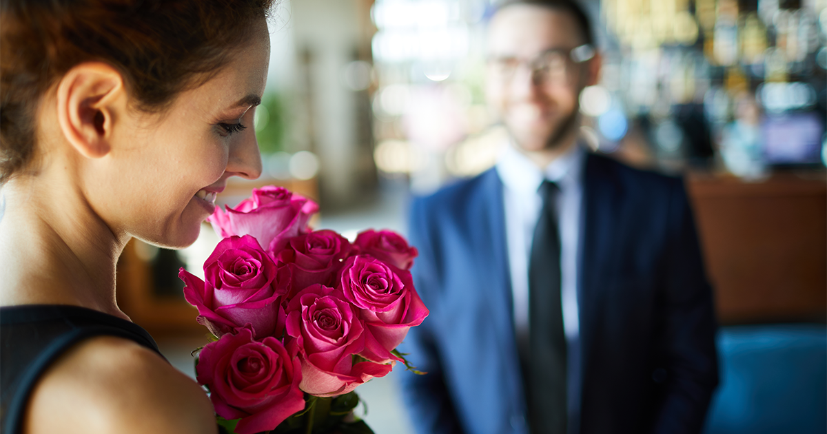 Woman holding roses, with man in the background. 